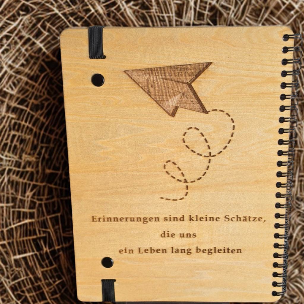 Holz-Rückseite des Erinnerungsbuchs mit der Gravur „Erinnerungen sind kleine Schätze, die uns ein Leben lang begleiten“ und Papierflieger-Motiv.