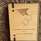 Holz-Rückseite des Erinnerungsbuchs mit der Gravur „Erinnerungen sind kleine Schätze, die uns ein Leben lang begleiten“ und Papierflieger-Motiv.
