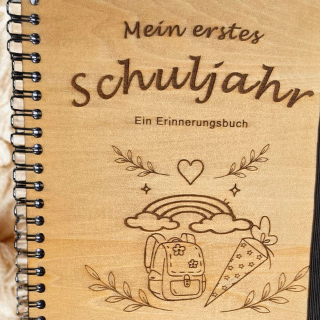 Personalisiertes Einschulungsbuch aus Holz mit Wunschnamen Amelie, Regenbogen- und Schultüten-Gravur, schwarzer Spiralbindung und Holz-Kugelschreiber.