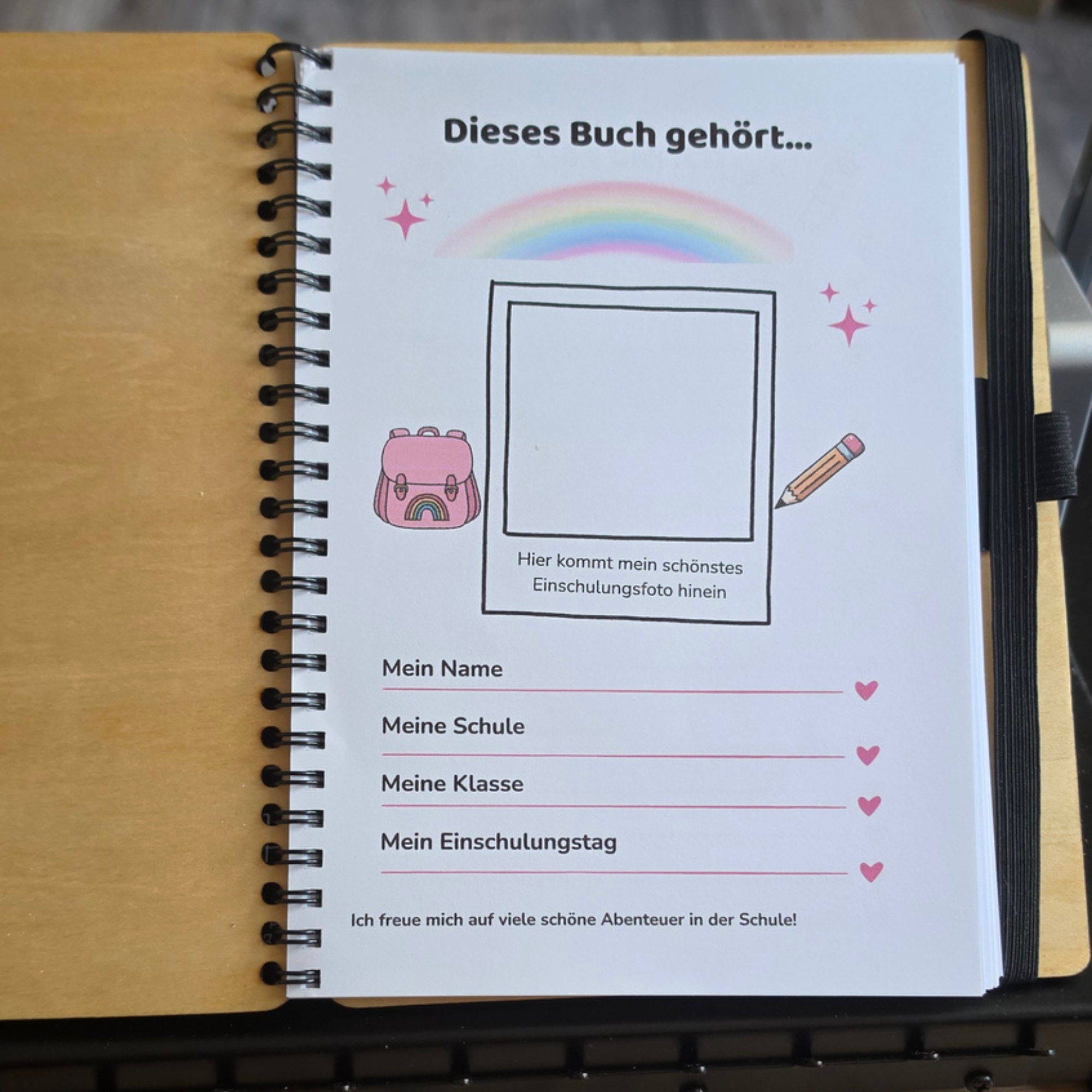 Aufgeschlagenes Erinnerungsbuch zur Einschulung mit farbig gestalteter Ausfüllseite, Platz für ein Erinnerungsfoto und Zeilen für eigene Notizen.